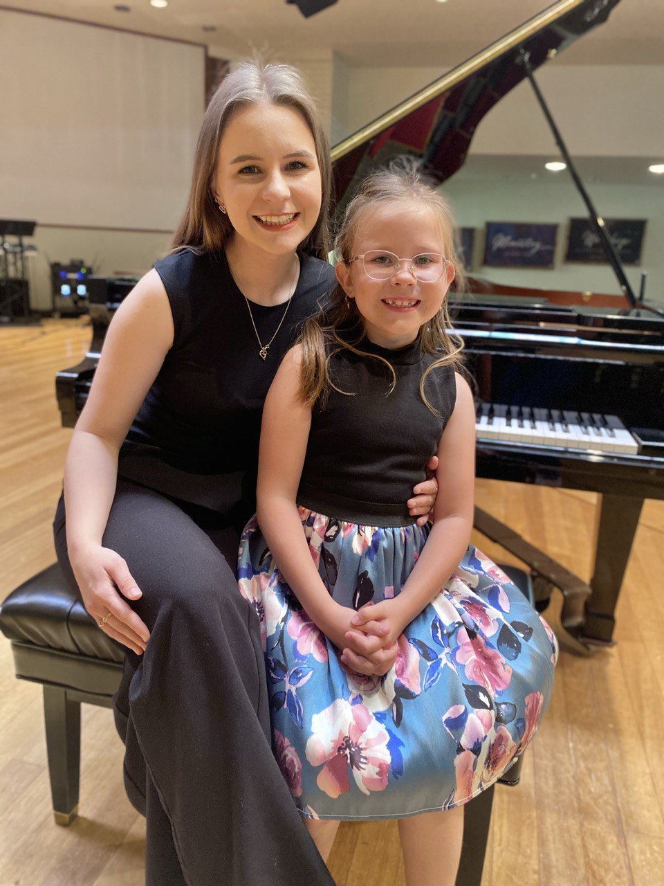 Anastasiia seated with a young piano student beside a grand piano