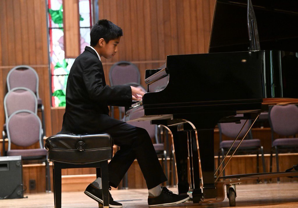 Piano student performing on a grand piano at a recital
