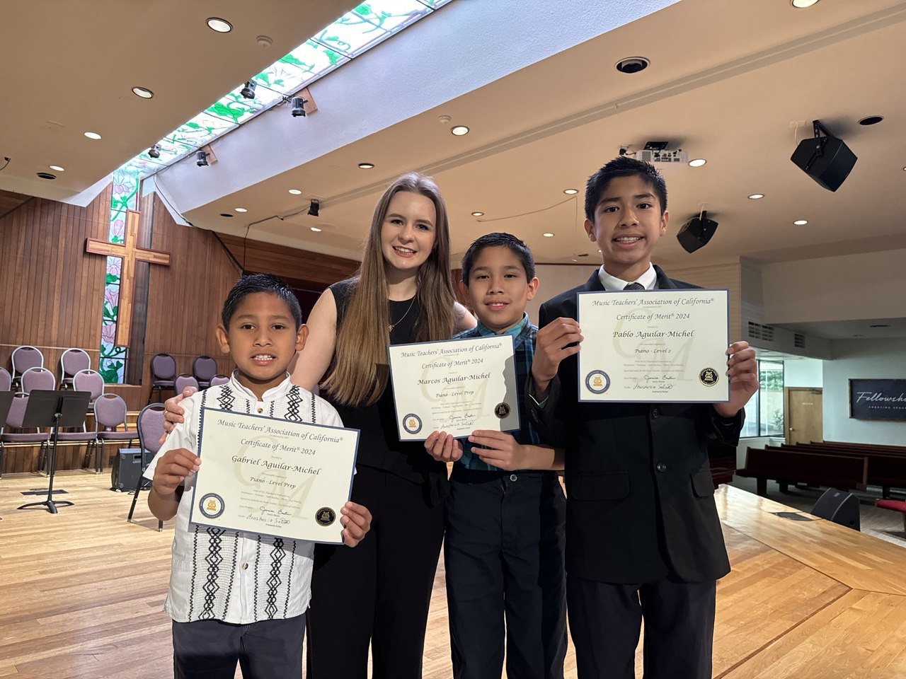 Anastasiia and three piano students holding certificates after a recital